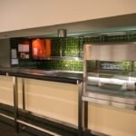 An empty commercial kitchen space with green tiles and stainless steel counters