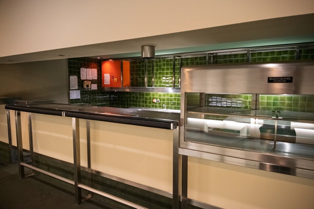 An empty commercial kitchen space with green tiles and stainless steel counters