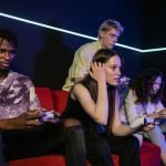 Group of friends enjoying a gaming session on a red sofa with wireless controllers. — Leading Sports Card & Collectibles